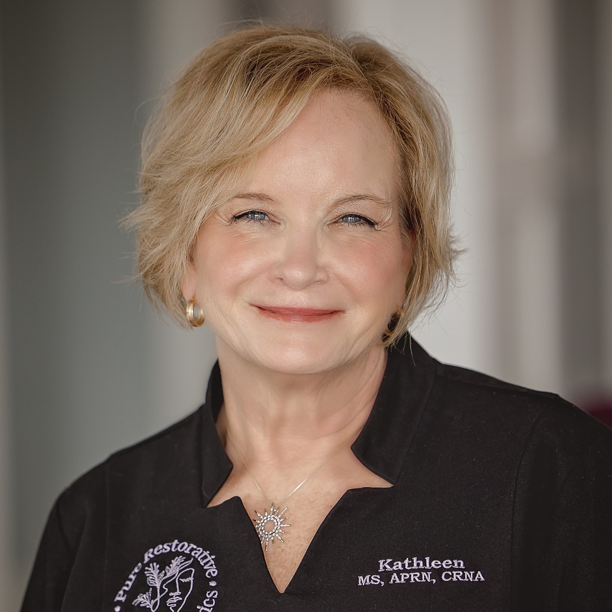 Kathleen wearing a black shirt with embroidered name and title, smiling in professional attire.