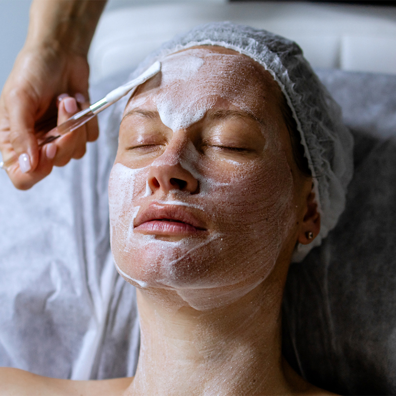 A person receiving a facial treatment with a white mask applied.
