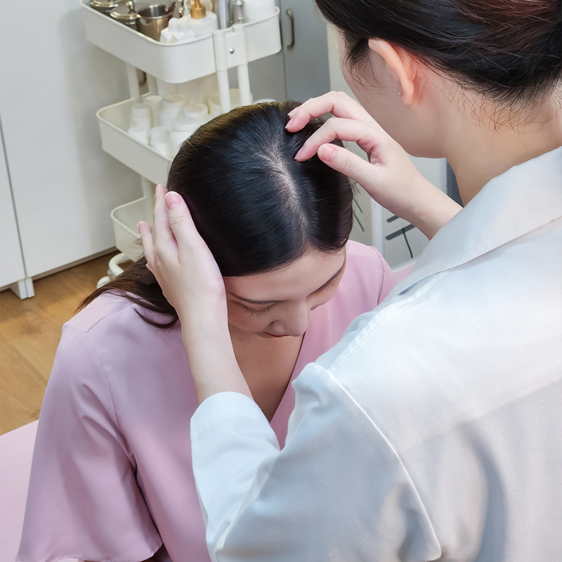 Haircare specialist examining a woman's scalp in a clinic.