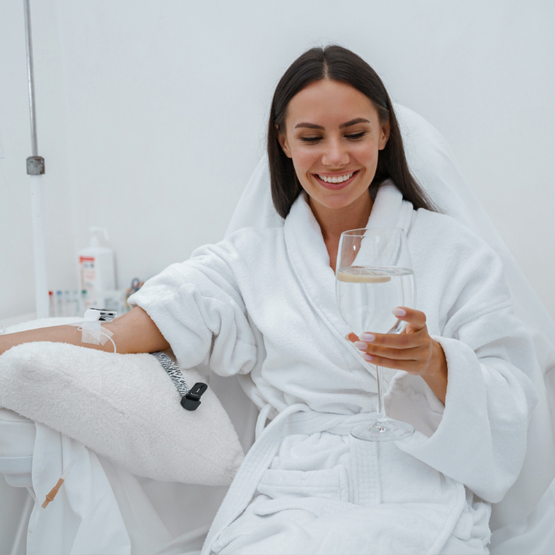A woman in a robe smiles while holding a glass of water during a wellness treatment.