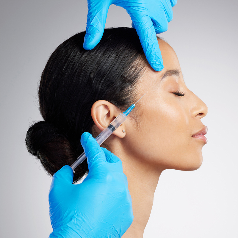 Gloved hands administering cosmetic injection on woman’s face.
