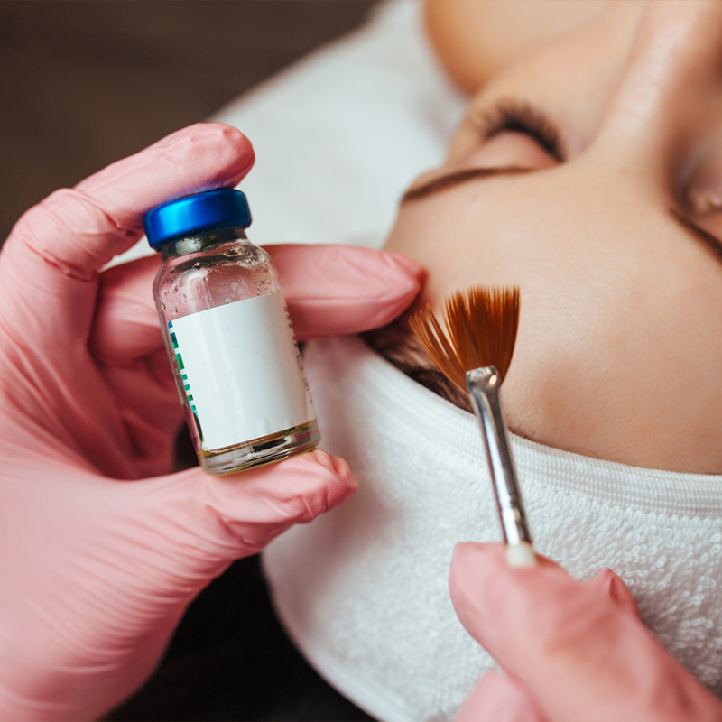 Applying facial treatment with a brush and serum in a salon setting.