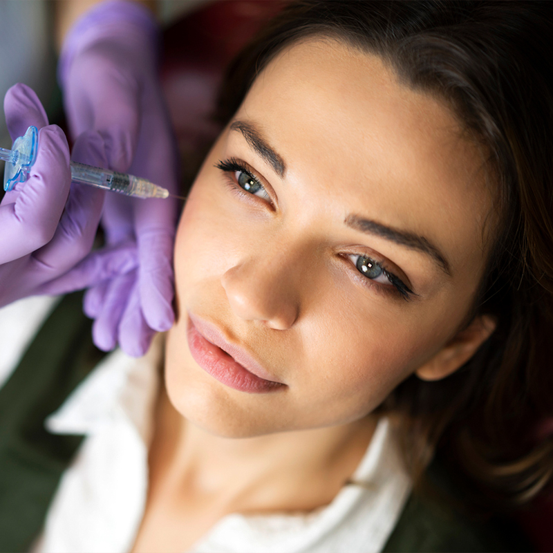 A woman receiving a cosmetic injection under eye by gloved professional.