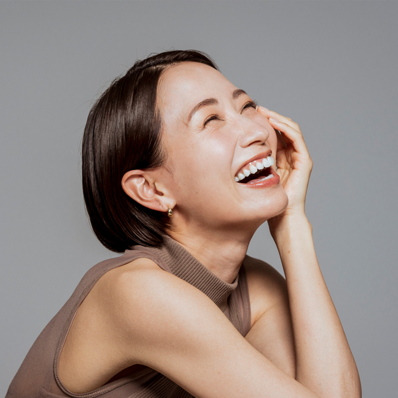 A woman laughing joyfully with a hand on her face.