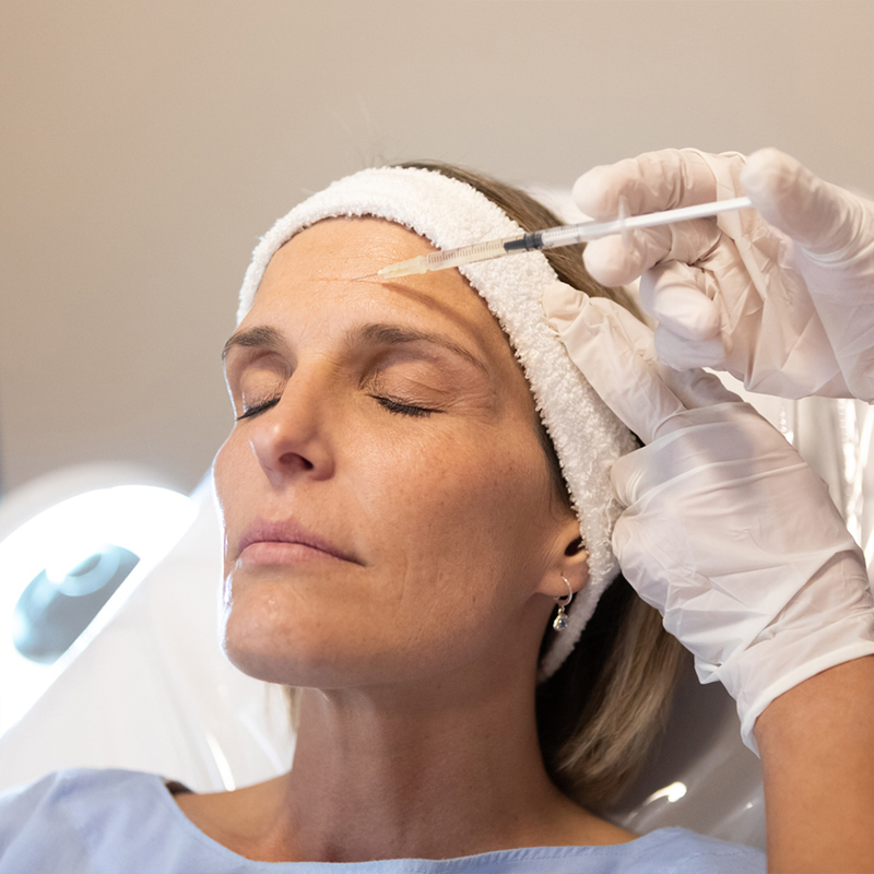 A woman receives a cosmetic forehead injection in a clinic setting.