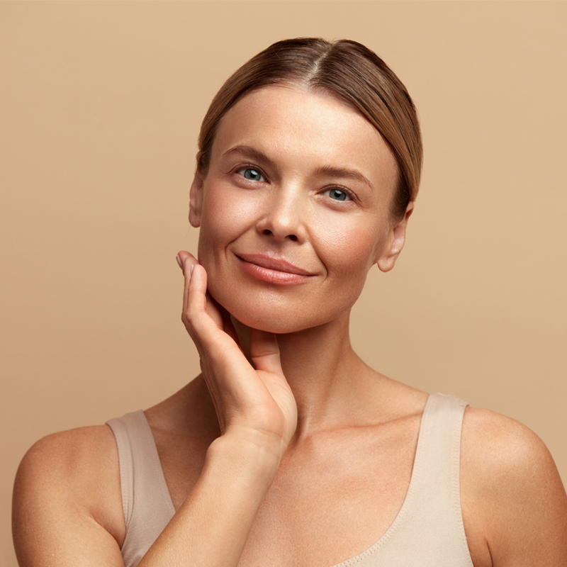 A woman with her hand on her cheek, smiling against a beige background.