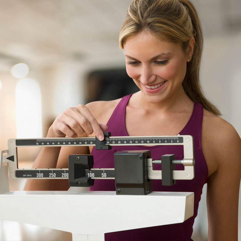 A woman adjusting a mechanical scale while smiling in a gym setting.