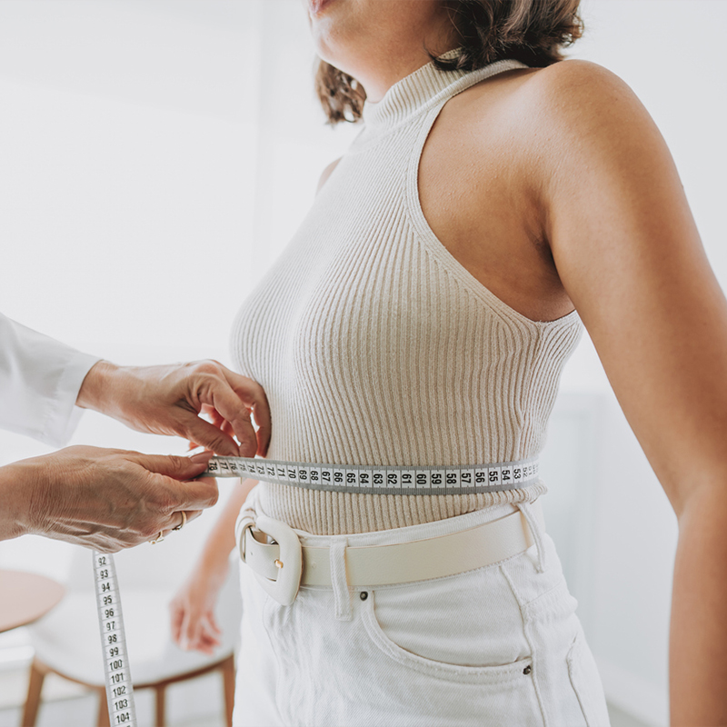 Person getting waist measured with tape for clothing fit in a bright room.